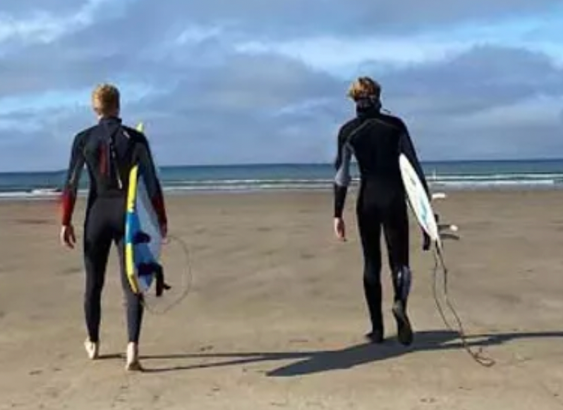 Tom Martlew and business partner, Nic, walking to sea with surfboards